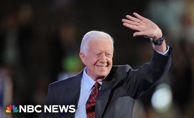 Historyczne zdjęcie Jimmy'ego Cartera uściskającego dłoń Menachema Begina i Anwara Sadata w Camp David, symbolizujące porozumienia pokojowe.