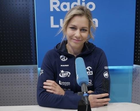 Alt: Aleksandra Mirosław w stroju sportowym, uśmiechnięta, stojąca obok ścianki wspinaczkowej, symbolizująca jej zaangażowanie w treningi i pasję do wspinaczki.