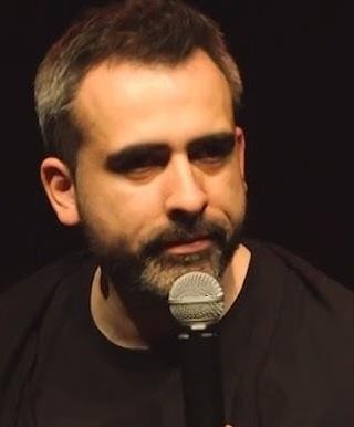 Abelard Giza na scenie podczas występu stand-upowego, dynamiczna poza z mikrofonem, teatralne oświetlenie.