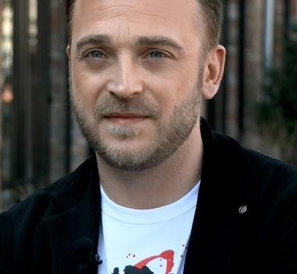 Mateusz Gessler w akcji w profesjonalnej kuchni, skupiony na przygotowywaniu potrawy, z elementami restauracji w tle.