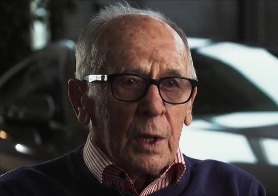 Sobiesław Zasada w klasycznym samochodzie rajdowym (np. Porsche 911), dynamicznie pokonujący trasę rajdu, z kurzem w tle, symbolizujący jego mistrzostwo i pasję do wyścigów.