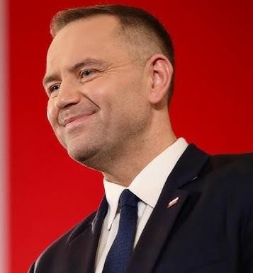 Karol Nawrocki, prezes IPN, przemawia na uroczystości historycznej, w tle widoczny tłum i polskie flagi.