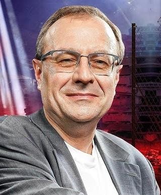 Antoni Dudek podczas wystąpienia publicznego, z gestykulacją, na tle sugerującym studio telewizyjne lub wykładowe, podkreślający jego rolę jako publicysty i popularyzatora historii.