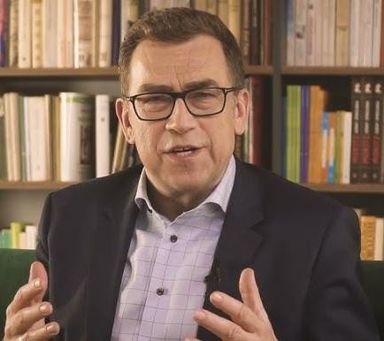 Maciej Orłoś w trakcie wystąpienia publicznego lub prezentacji, z otwartą postawą, podkreślającą jego rolę jako mówcy i szkoleniowca.