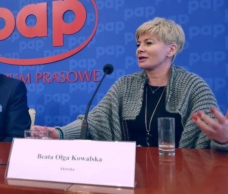 Beata Olga Kowalska na scenie, w trakcie ekspresyjnego występu teatralnego lub musicalowego, z dynamicznym oświetleniem podkreślającym nastrój.