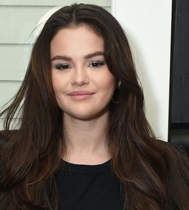 Selena Gomez na scenie podczas koncertu, śpiewająca z mikrofonem, w otoczeniu świateł scenicznych i rozmytego tłumu, oddająca energię i pasję występu na żywo.