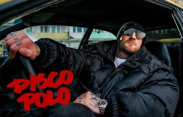 Kizo podczas energetycznego występu na scenie, z mikrofonem w dłoni, w otoczeniu świateł koncertowych.