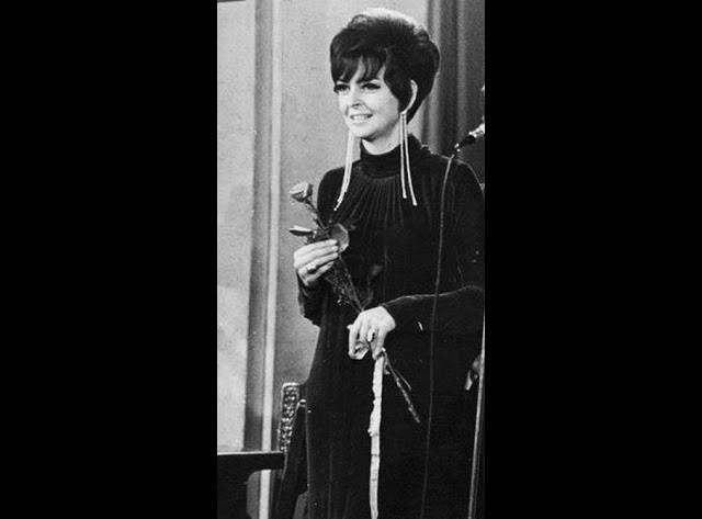 Rena Rolska podczas występu na scenie, śpiewająca do mikrofonu, w stylizacji z lat 60. lub 70. XX wieku.